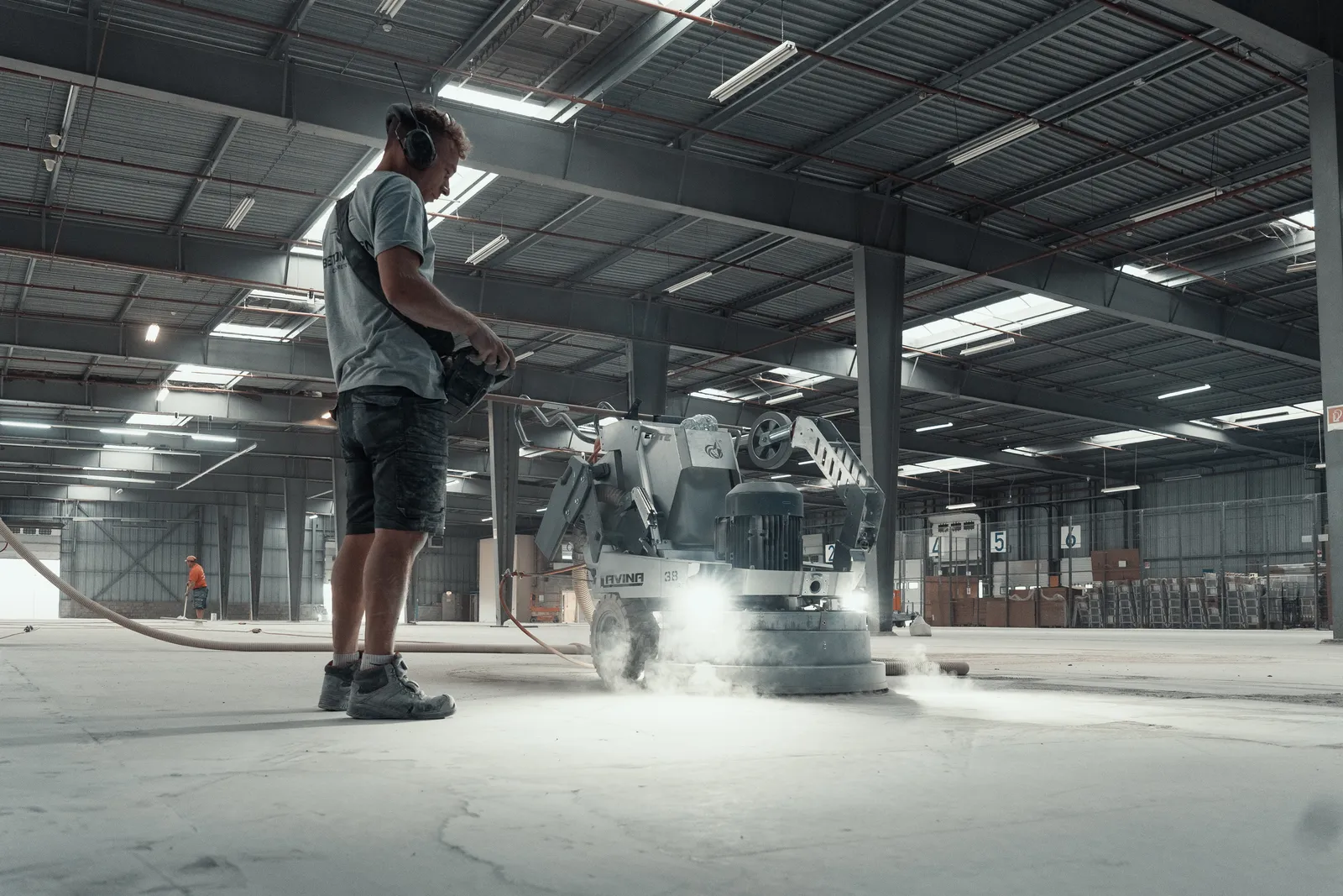Betonvloer schuren door Beton Design Vakman van Beton Design schuurt een betonvloer in een magazijn met een diamantschuurmachine